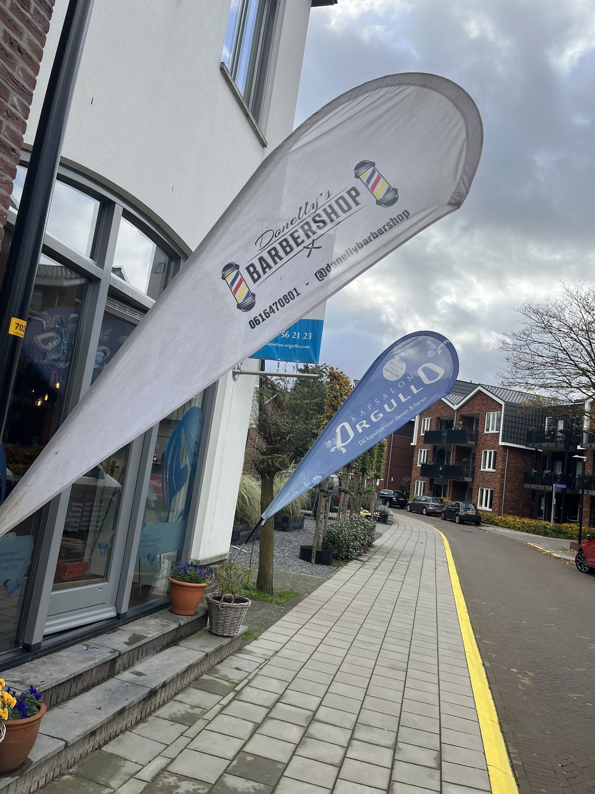 Een vlag van Donelly's Barbershop naast een vlag van Orgullo voor de salon